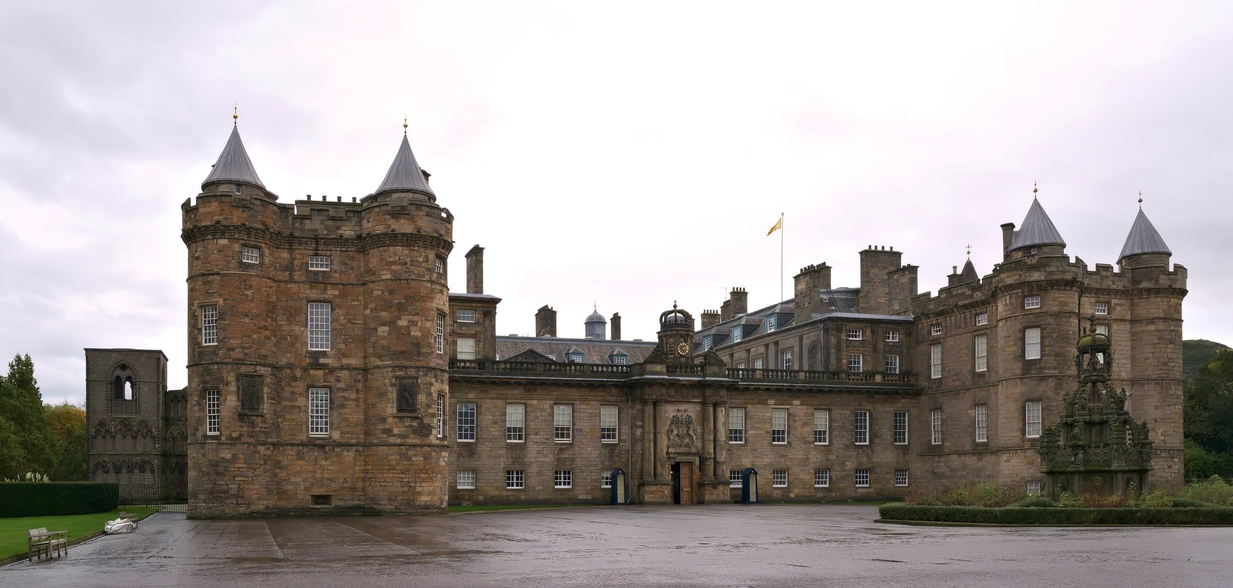 Palace of Holyroodhouse facade with two round towers, a central gateway and an ornate fountain at the right.