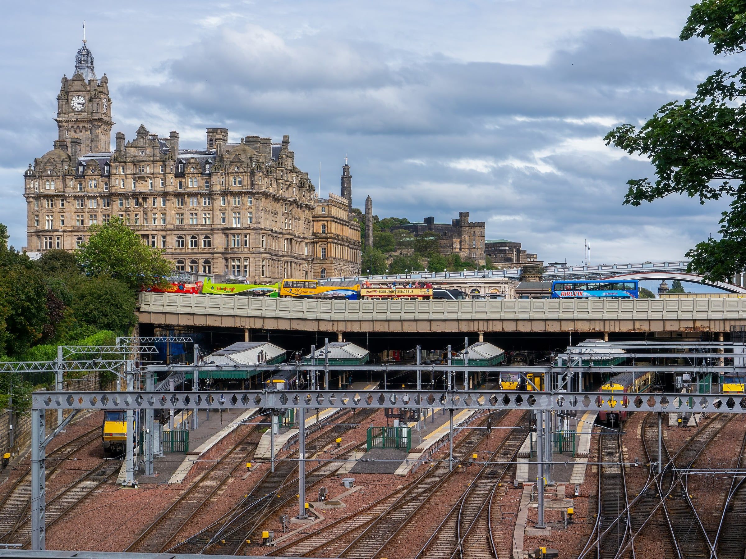 Edinburgh Waverley station's railway tracks and platforms, with the Balmoral Hotel clock tower and castle beyond.